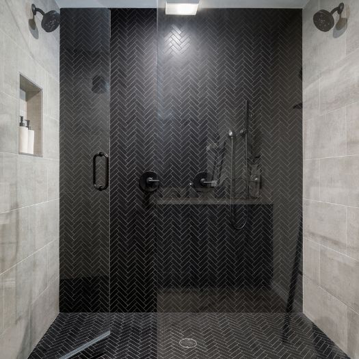 Modern shower with black herringbone tile, dual shower heads, and built-in shelving.