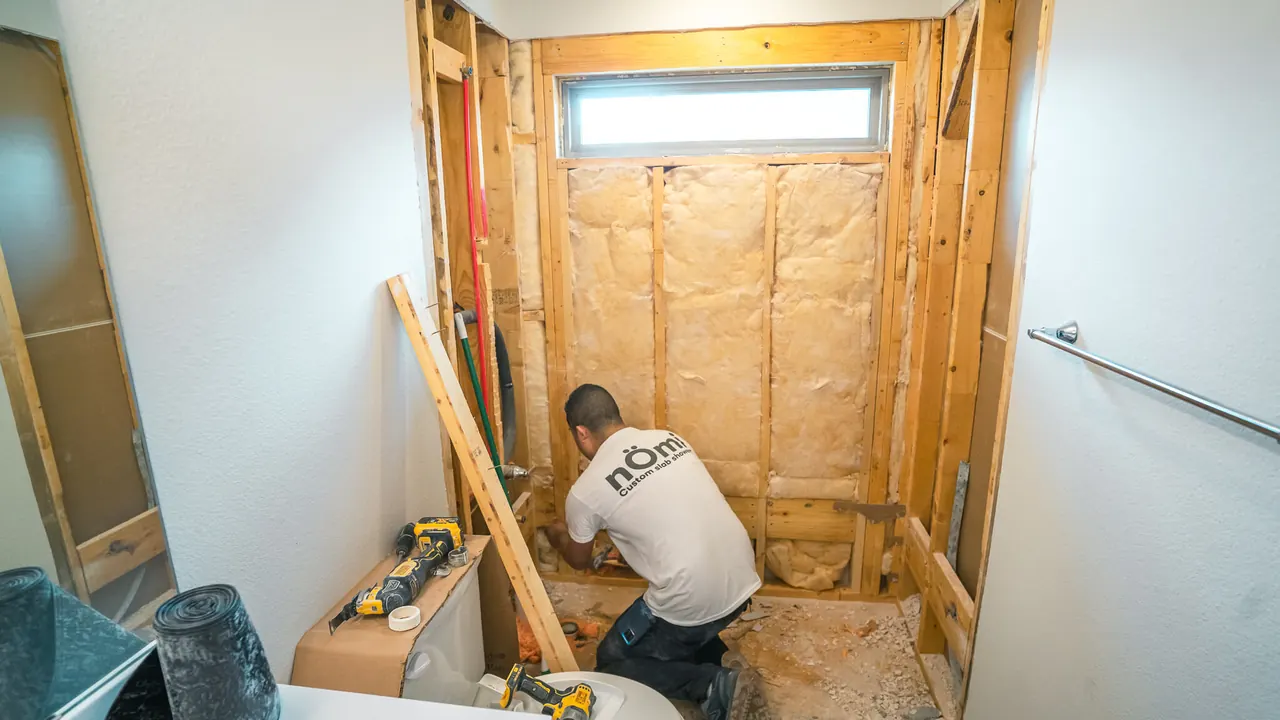 Nomi crew member framing a bathroom wall after demolition, with the room opened down to the studs