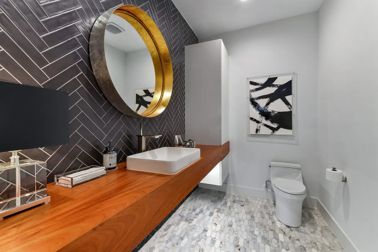 Denton bathroom remodel idea: floating wood vanity, round brass mirror and a charcoal herringbone wall