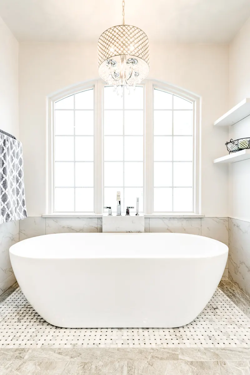 Highland Park bathroom remodel idea: freestanding tub under an arched window with a chandelier