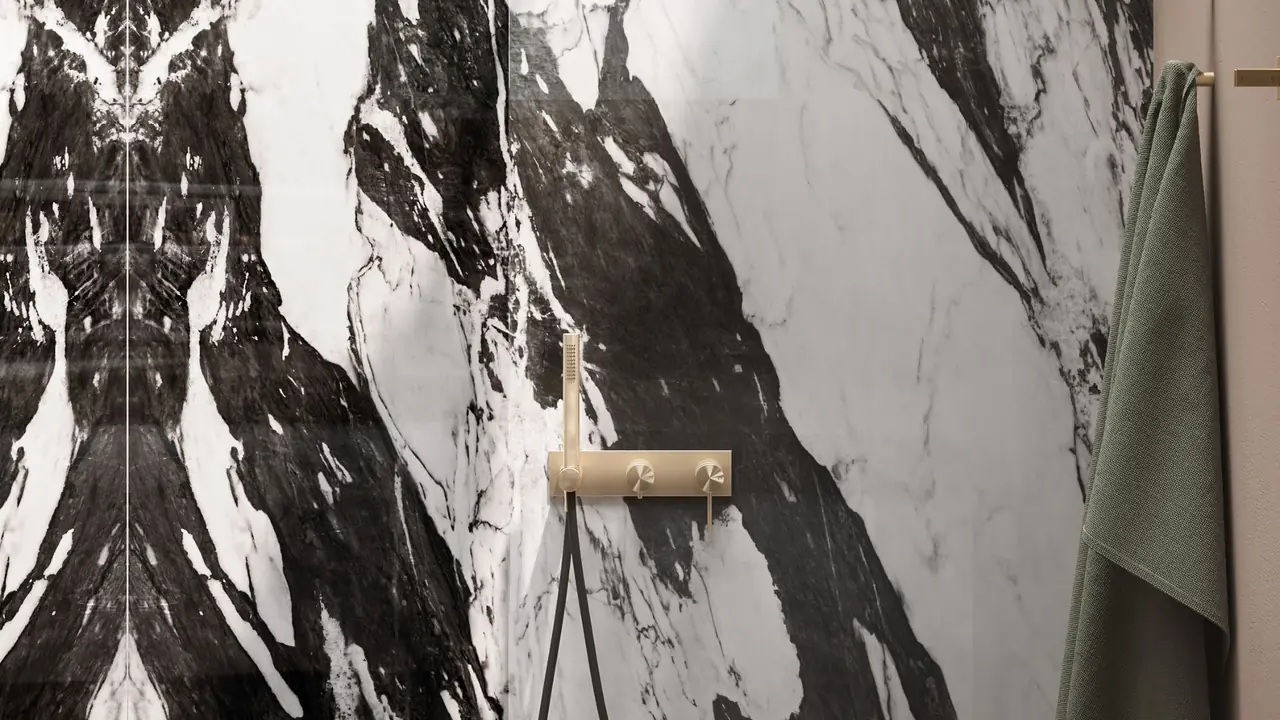 Luxury bathroom remodel in Dallas by Nomi, a bookmatched black and white marble shower with a brushed brass shower set