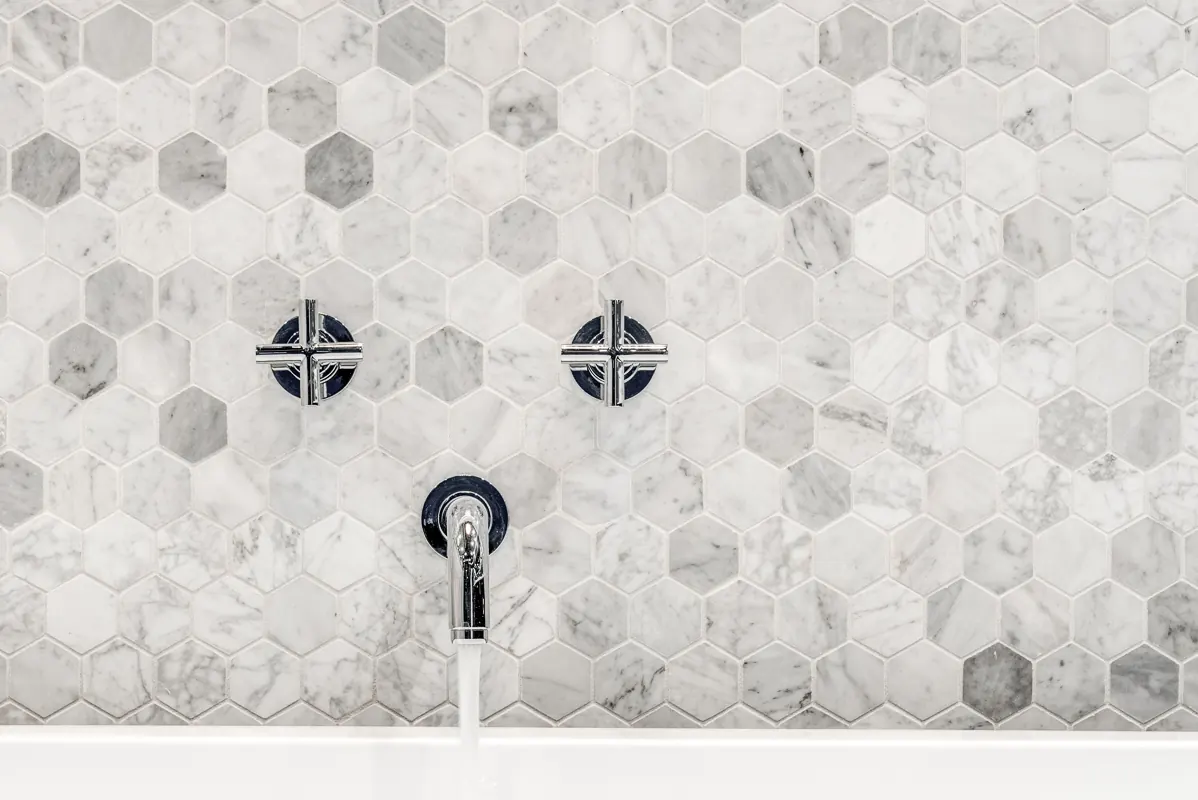 White marble hexagon tile wall with matte black cross handles and a wall-mounted spout