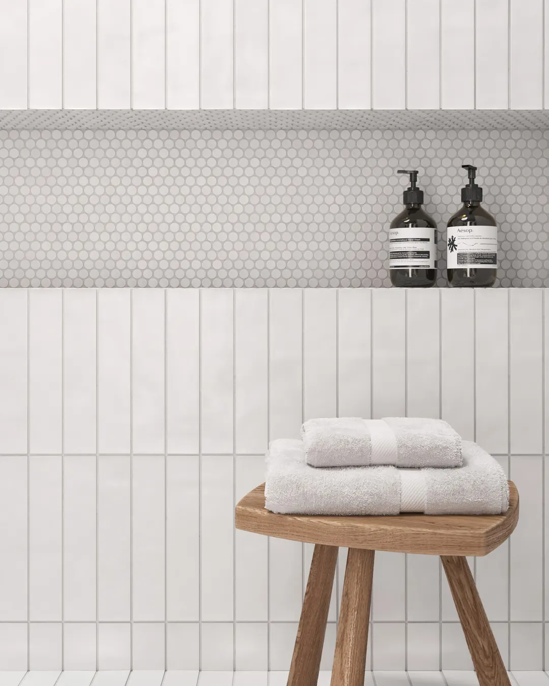 Shower in white vertical stacked tile with a penny tile niche and a wooden stool