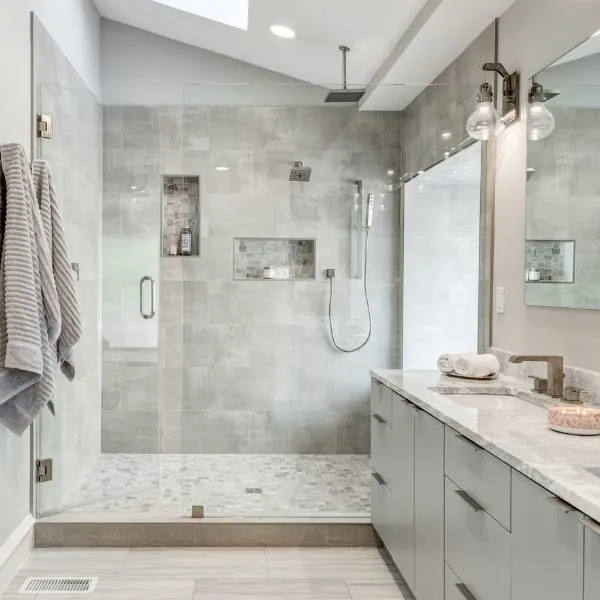 Walk-in shower in gray tile with two niches and a rain head, beside a marble-topped vanity