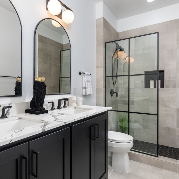 Modern bathroom featuring a double vanity with marble countertop, black fixtures, and a walk-in shower with glass enclosure.